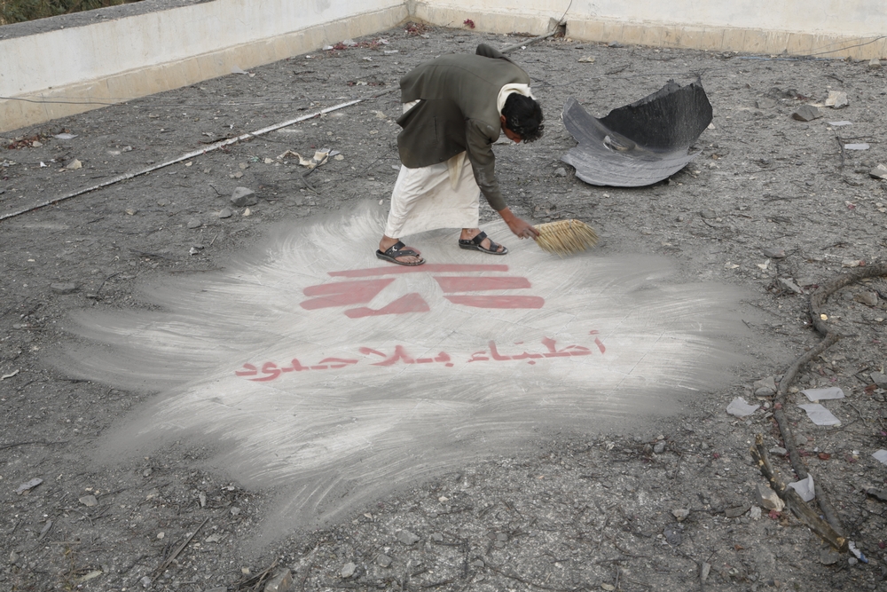 A man sweeping away dirt from an MSF logo at his feet.