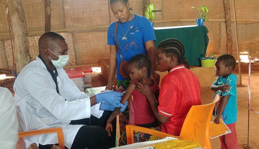 An MSF medic wearing a face mask and gloves while vaccinating a child