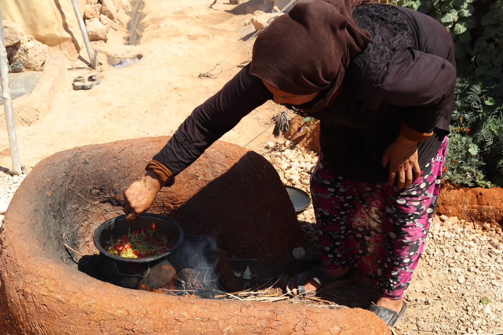 Displaced woman cooking for lunch on woodfire outside her tent in a displacement camp in northwest Syria.