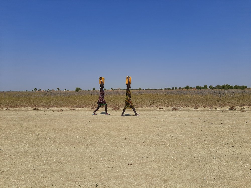 Women in Riang, Jonglei State, walk around the community carrying water containers.