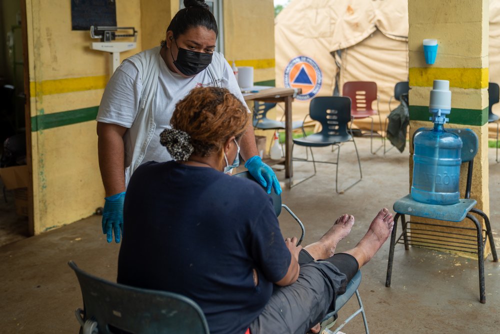 Lucero, an MSF nurse, listens to a patient while the patient keeps her feet up. (June, 2021).