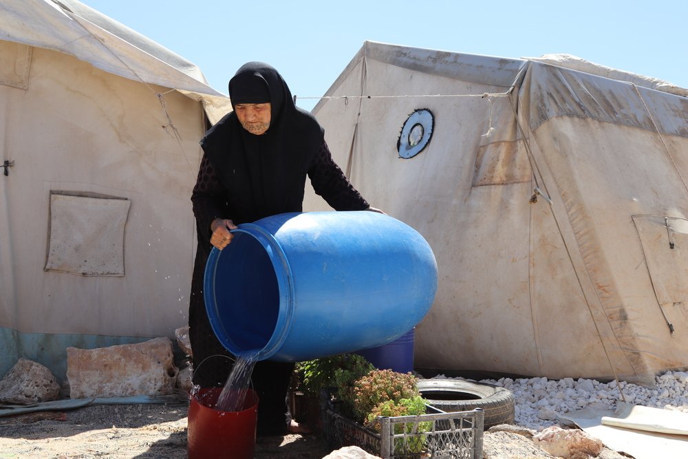 An old displaced woman filling a bucket with clean water provided by MSF in a camp in northwest Syria.