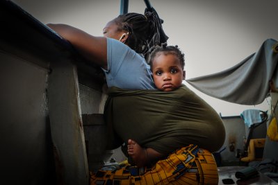 A mum and baby look towards the shore of Sicily as they prepare to disembark from the Sea-Watch 4 following their rescue in August 2020.