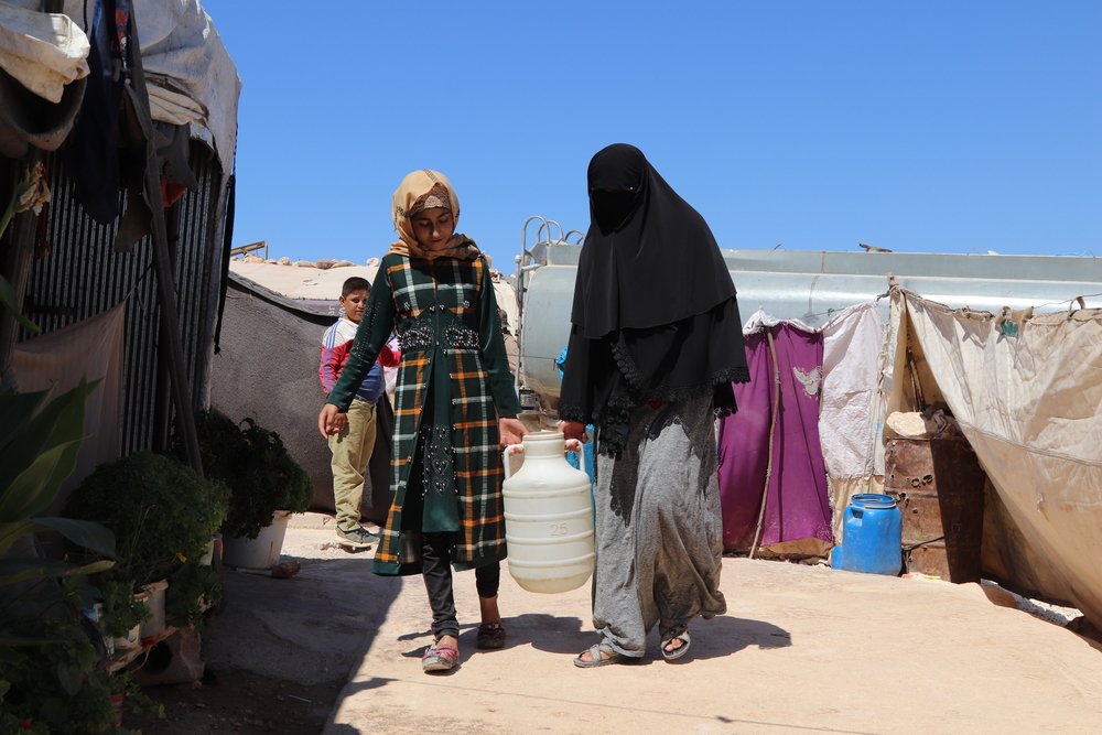 Displaced women carrying a pail of clean water provided by MSF in a camp in northwest Syria.