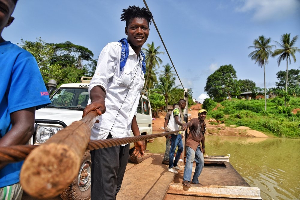 Ferry worker transports MSF vehicle across Sewa river in Kenema district eastern Sierra Leone. People, cars and goods are transported across this ferry and the worker uses a wooden stick that pulls an iron rope.