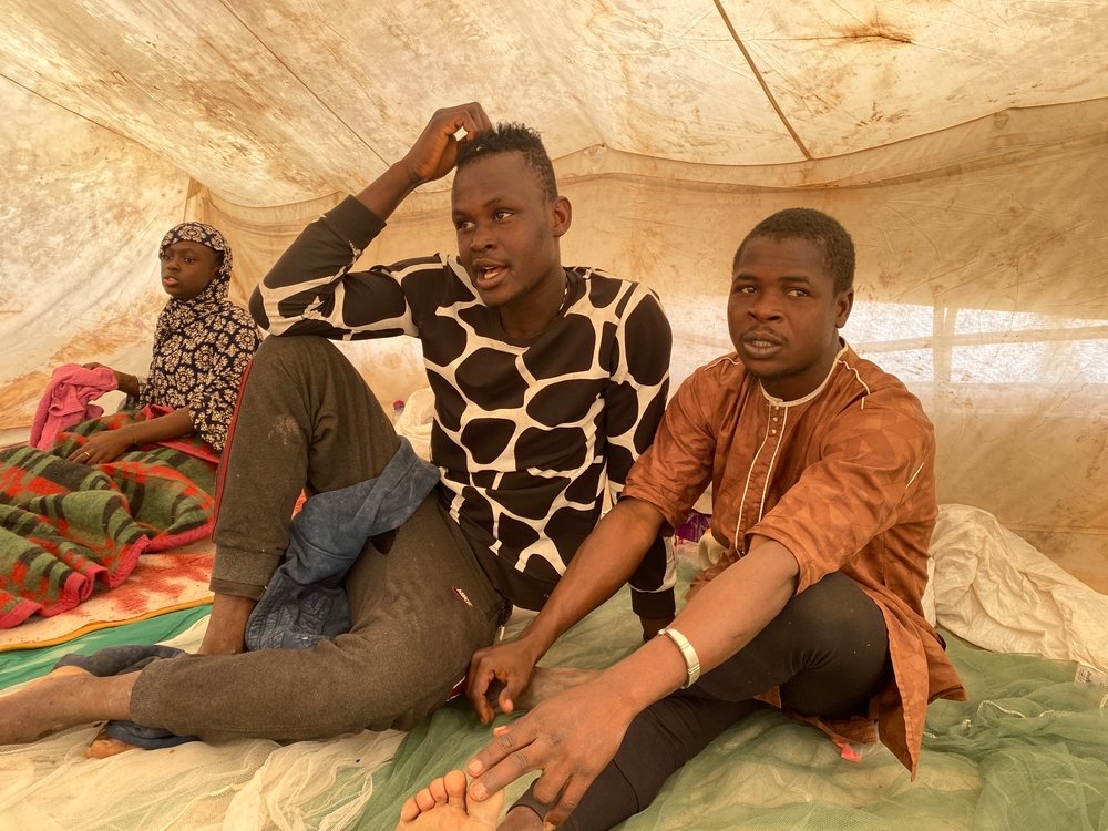 Three migrants – a woman and two men – sit in the tent where they are staying in Assamaka.