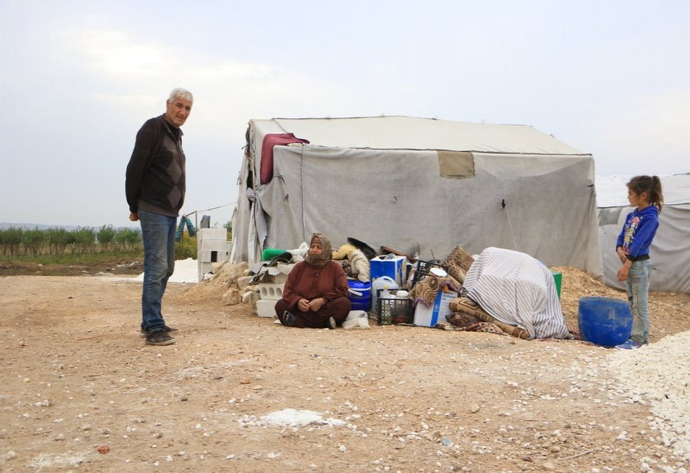 A displaced family sitting next to their luggage outside while waiting the isolation of their tent to be done.