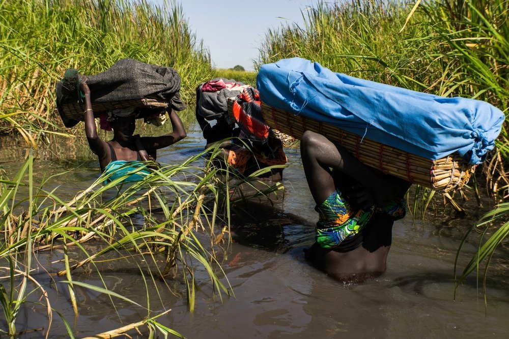 Woman pass each other while wading through the swamps from Kok Island trying to reach Thonyor in time to receive food distribution for the first time since 5 months in the troubled Unity State in South Sudan. December 2013 - 2015.