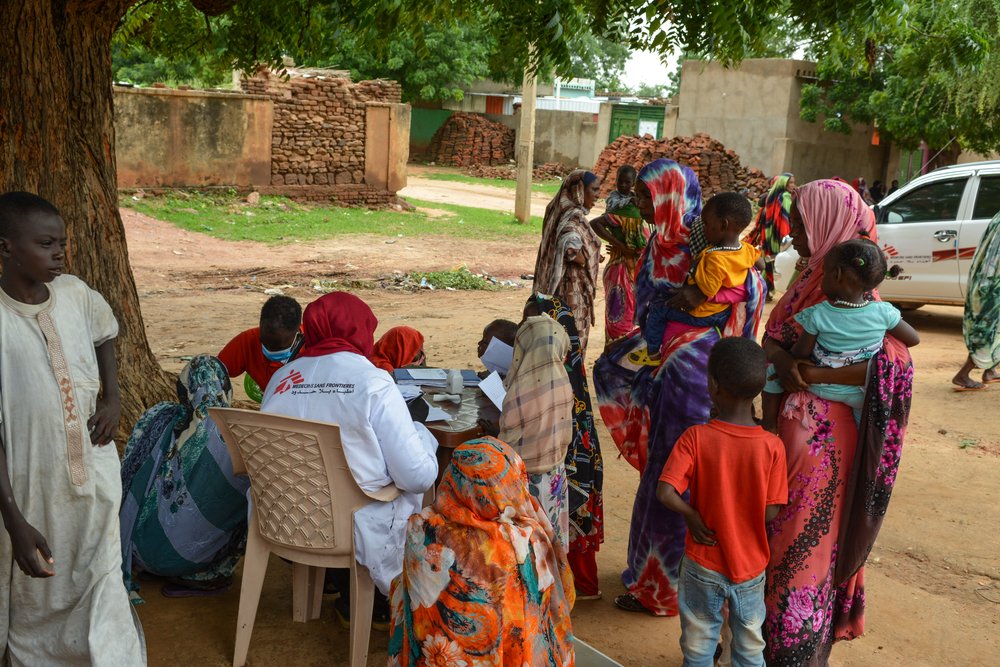 Patients gather around a consultation table at MSF’s mobile clinic in  Al-Nasim, Al-Geneina. 