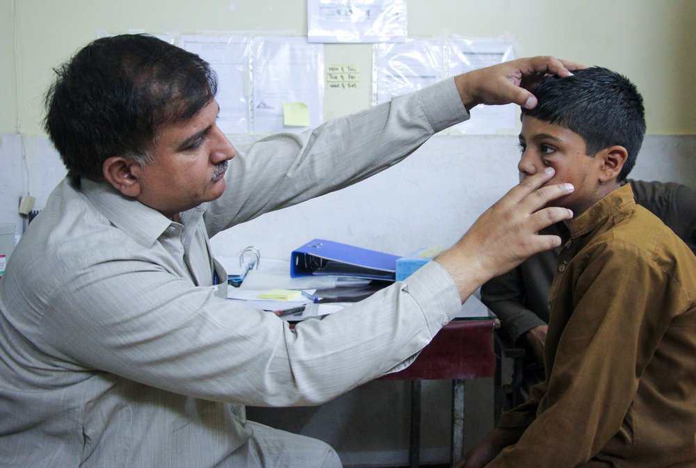 A supervisor for MSF cutaneous leishmaniasis treatment centre in Peshawar, Faqeer Hussain, examines 11-year-old patient Mohammad Asif’s lesion under the eye. Pakistan, 2020.