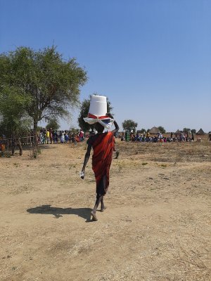 A mother walks back home carrying a kit donated by MSF containing mosquito nets, blankets, buckets, soap, water purifiers and filters, a plastic sheet and rope.