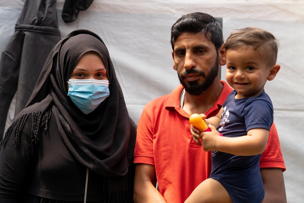 Portrait photo of Jaber Alsoudy, his wife and child outside their tent. Jaber, 37, and his wife, 21 years old, left from Syria because of the war, seeking for a safe place and a better future in Europe. During the journey his wife was heavily pregnant.
