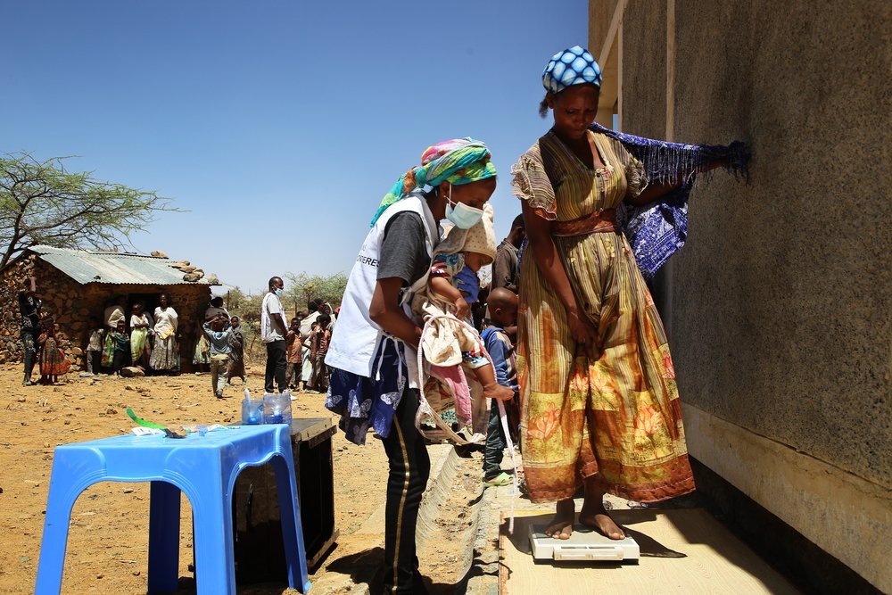 MSF staff member holds a child while her mother is weighed during a mobile clinic in the village of Adiftaw, in the northern Ethiopian region of Tigray.