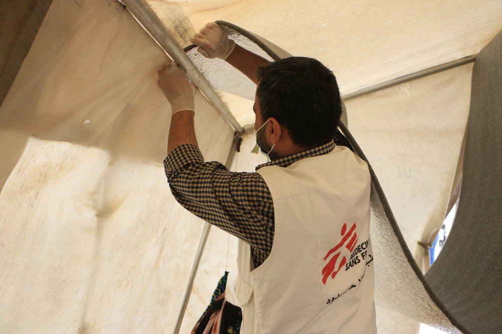 MSF logistics staff are installing tent roof isolation and a thermal insulator inside a tent.
