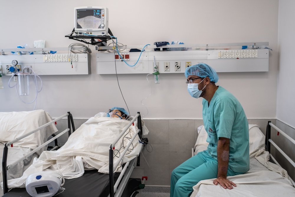 A nurse sits with four-year-old Hala in the Al-Awda hospital limb reconstruction unit recovery room, monitoring her vital signs as she wakes from having surgery on her foot, which was badly damaged in a car accident.