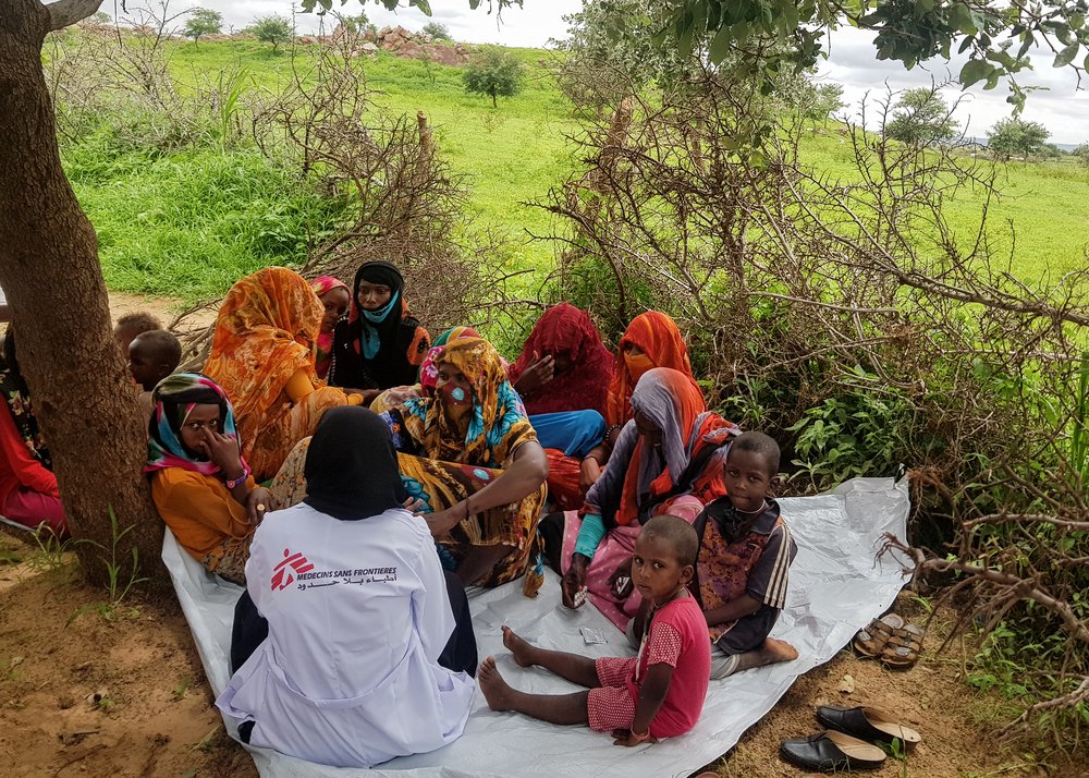 Patients gather around an MSF staff member at a mobile clinic outside Al-Geneina, aimed at reaching communities unable to access healthcare inside the city.