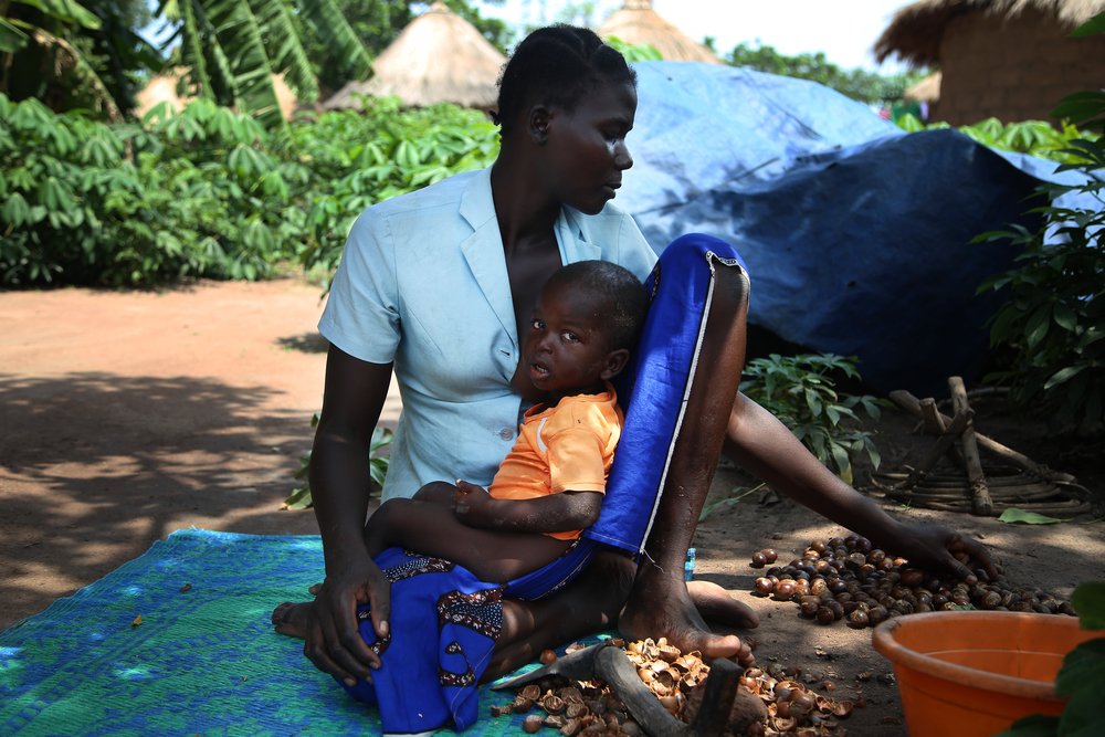 A woman holds a child, while she peals karité (shea) nuts at site B for displaced people in Kabo, a town in northern Central African Republic.