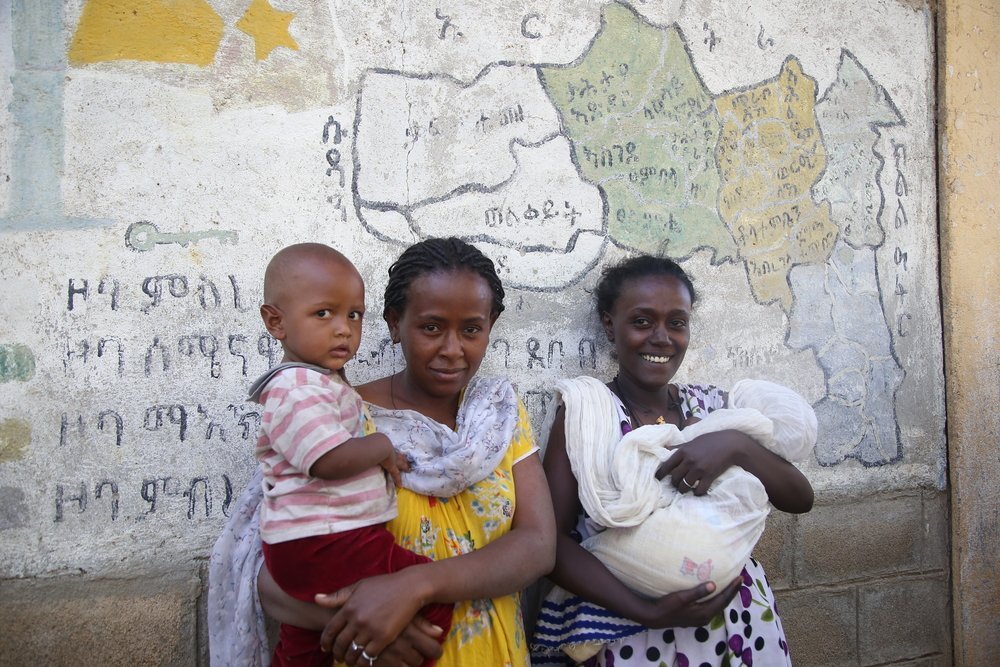 Sesel Gorohat, from Sheraro, with her two-year-old daughter, and Salam, from Humera, with her four-month-old baby, stand in front of a map of the Tigray region at the Basin school in Axum.