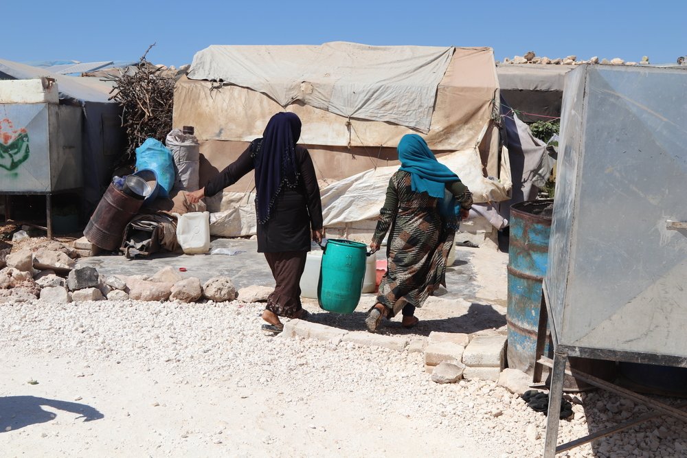 Displaced women are carrying a pail of clean water provided by MSF in a camp in northwest Syria.