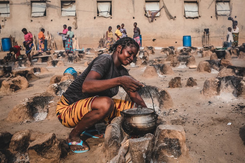 A young woman cooks an evening meal for her family in an open-air cooking area Abagana camp. 