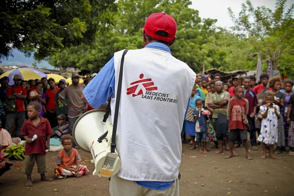 An MSF worker with a bullhorn stands in front of a crowd of locals.