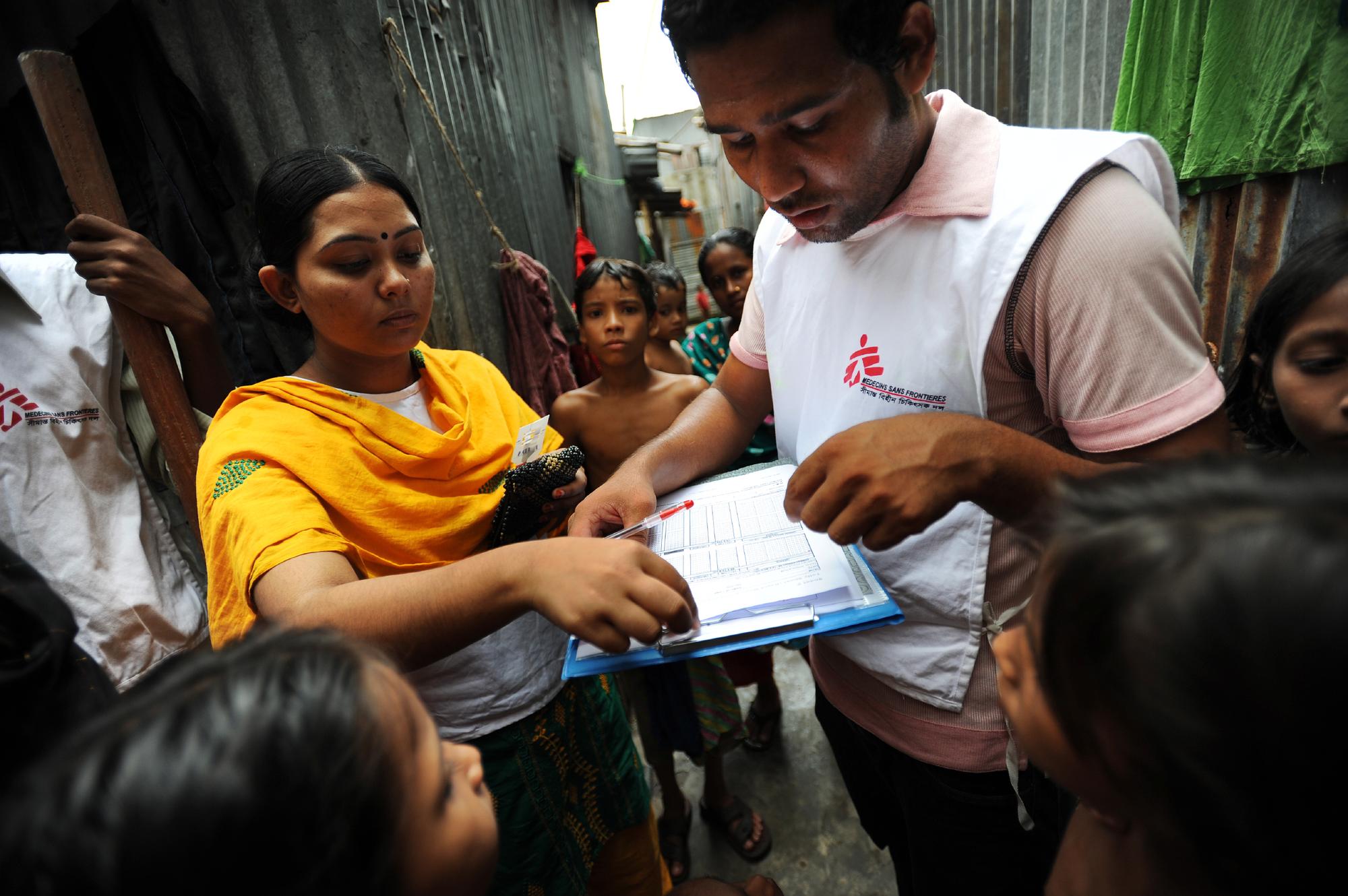 An MSF worker surrounded by people looks at a clip board.