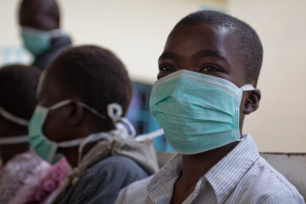 A boy wearing a surgical mask smiles.