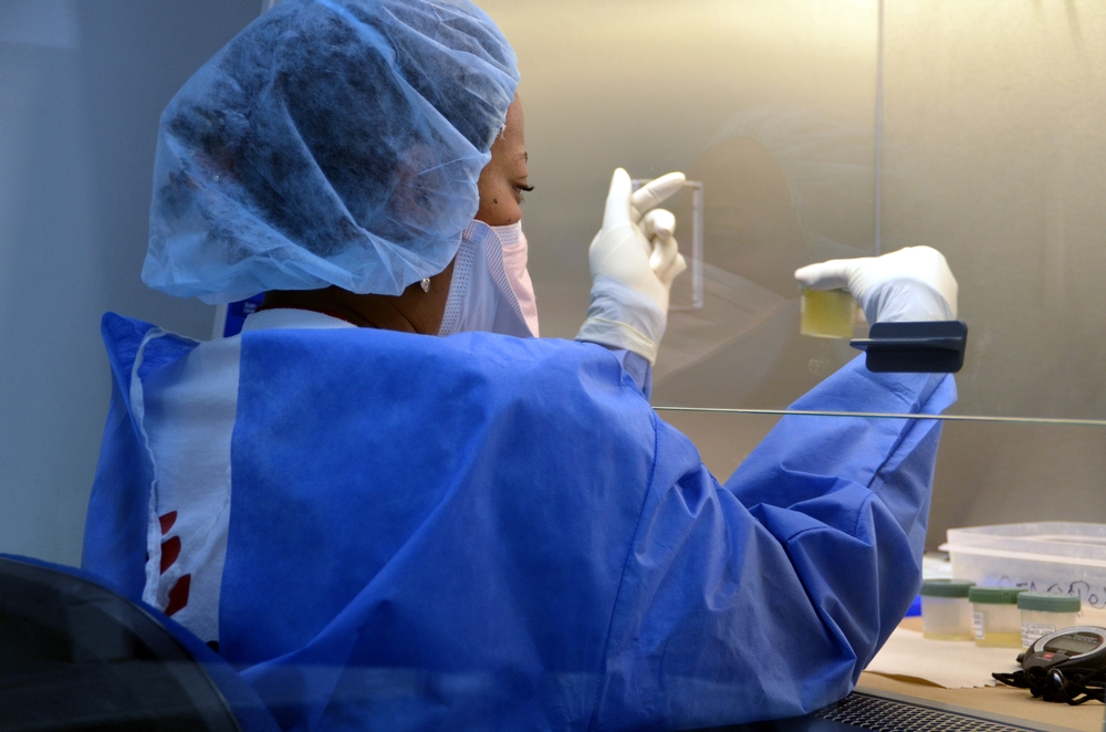 A woman wearing surgical protective clothing holds up a container in a bio safety cabinet.