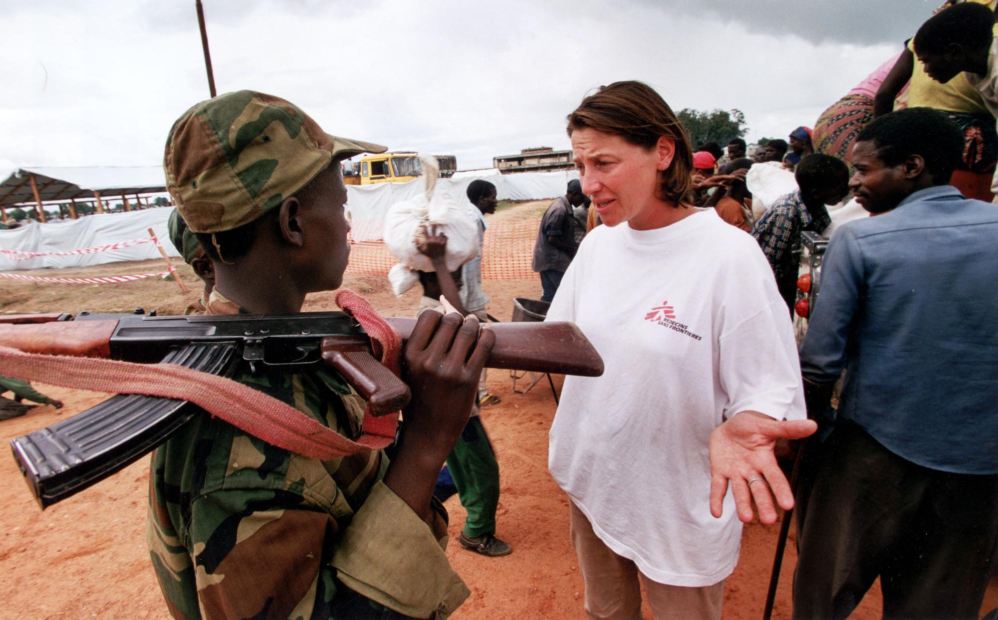 An MSF worker talks to an armed soldier in front of a line of people.